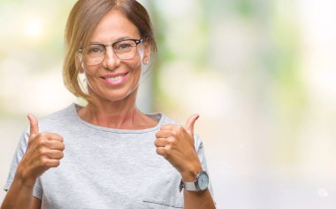 El ile pozitif jest yapıyor izole arka plan başarı işareti üzerinde gözlük takan orta yaş İspanyol kadın kıdemli başparmak gülümseyen ve mutlu. Neşeli bir ifadeyle, kazanan jest kameraya bakıyor.