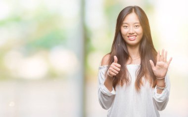 Genç Asyalı kadın gösterilen ve parmakları ile işaret izole arka plan üzerinde kendinden emin ve mutlu gülümseyerek süre 6 numara.