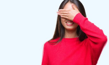 Genç Asyalı kadın gülümsüyor ve gözleri için sürpriz kapsayan yüz el ile gülüyor izole arka plan üzerinde kış kazak giyiyor. Kör kavramı.