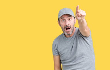 Yakışıklı orta yaş ağarmış komuta sizde üzerinde spor şapkası izole arka plan ile sürpriz devam parmakla, açık ağız hayret ifadesi, önünde bir şey