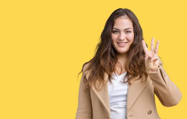 Parmakları ile kendinden emin ve mutlu gülümseyerek süre güzel artı boyutu genç kadın giyiyor kış ceket ve yukarıyı gösteren izole arka plan üzerinde üçüncüsü.