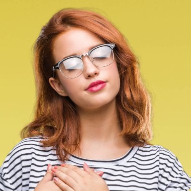 İzole arka plan ile gülümseyen gözlüklü genç güzel kadın kapalı gözler ve yüzünde minnettar jest ile göğüs üzerinde eller. Sağlık kavramı.