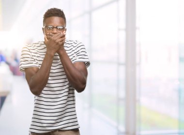 Gözlük ve lacivert t-shirt ağız hata için elleriyle kapsayan şok giyen genç Afro-Amerikan adam. Gizli kavramı.