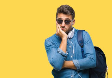 Kulaklıklar ve sırt çantası düşünme izole arka plan bakmaktan giyen genç yakışıklı turist adam yorgun ve sıkılmış çapraz silah depresyon sorunları ile.