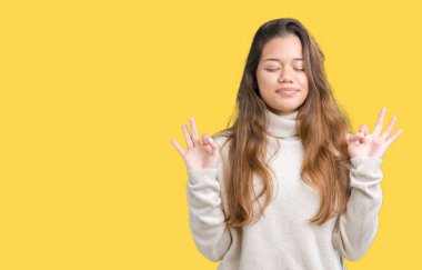 Genç güzel esmer kadın giyiyor boğazlı kazak izole arka plan üzerinde dinlenmek ve gülümseyen gözlerle kapalı parmak jestle meditasyon yapıyor. Yoga kavramı.