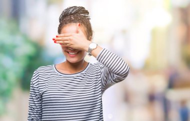 Genç örgülü saç Afro-Amerikan kız gülümsüyor ve gözleri için sürpriz kapsayan yüz el ile gülüyor izole arka plan üzerinde kazak giyiyor. Kör kavramı.