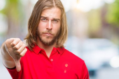 Mutsuz ve kızgın ret gösterilen ve başparmak aşağı hareketi ile negatif seyir izole arka plan üzerinde uzun saçlı Genç yakışıklı adam. Kötü ifade.