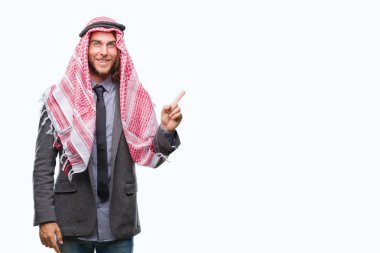 Uzun saçlı keffiyeh yüzünde kocaman bir gülümseme ile izole arka plan üzerinde giyen genç yakışıklı Arap adam kameraya bakarak yan el ve parmak ile işaret.