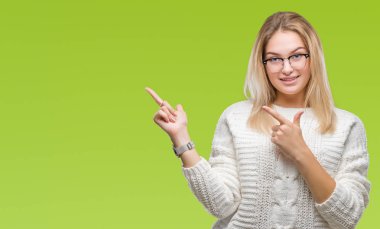 Gülümseyen ve iki elleri ve parmakları ile tarafına işaret kamera bakarak izole arka plan üzerinde gözlük takan genç kafkas kadın.