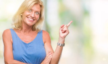 Kameraya bakarak yan el ve parmak ile işaret orta yaş sarışın kadın yüzünde kocaman bir gülümseme ile izole arka plan.