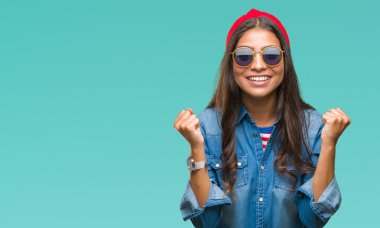 Genç güzel Arap kadın izole arka plan kutlama üzerinde güneş gözlüğü takıyor şaşırttı ve başarı için kaldırdı kollarını açarak hayret ve gözleri açık. Kazanan kavramı.