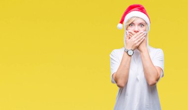 Üzerinde Noel şapka giyen genç güzel sarışın kadın arka plan ağız hata için elleriyle kapsayan şok izole. Gizli kavramı.