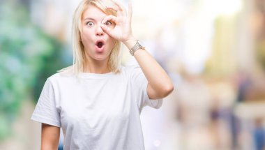 Sürpriz yüz, göz parmaklarının arasından seyir ile ok jest yapıyor izole arka plan üzerinde beyaz t-shirt giyen genç güzel sarışın kadın şok. İmansız ifade.