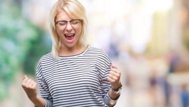 Genç güzel sarışın kadın üzerinde gözlük gülümseyen ve başarı için çığlık arka plan çok mutlu ve heyecanlı kaldırdı, silah ile kazanan jest yapıyor izole. Kutlama kavramı.