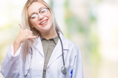 Genç sarışın doktor kadın yapıyor gülümseyen izole arka plan üzerinde telefon hareketi ile el ve parmak telefonda konuşuyor gibi. Kavramları iletişim.