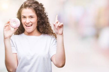 Genç esmer kız izole arka bir fikir ya da soru işaret parmağı gülen yüz, bir numara ile sürpriz üzerinde donut yemek