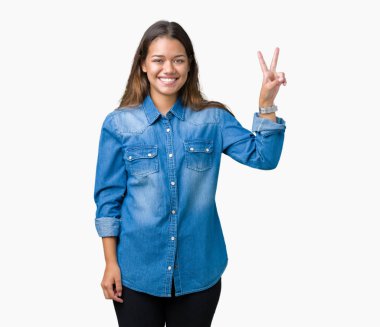 Mutlu yüz zafer işareti yaparken kameraya göz kırpıyor ile gülümseyen izole arka plan üzerinde mavi kot gömlek giyen genç güzel esmer kadın. İki numaralı.