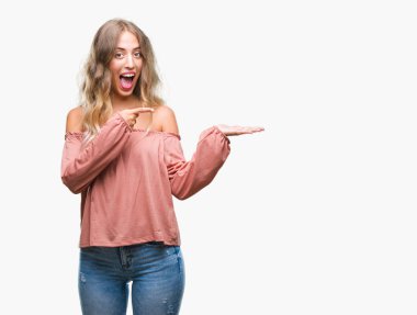 Hayret ve el ile sunulması ve parmak ile işaret ederken kameraya gülümseyen izole arka plan üzerinde sarışın güzel genç kadın.