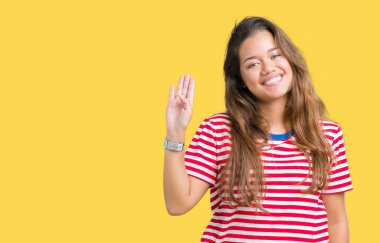 T-shirt üzerine izole arka plan Waiving Merhaba mutlu ve gülümseyen, dostça karşılama jest giyen genç güzel esmer kadın çizgili