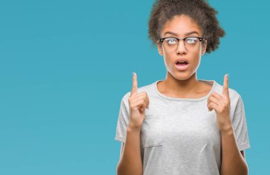 Genç afro Amerikalı kadın hayrete ve yukarıya bakıyor ve parmakları ile işaret ve silah kaldırdı sürpriz izole arka plan üzerinde gözlük.