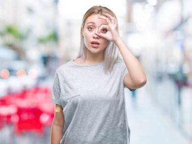 Sürpriz yüz, göz parmaklarının arasından seyir ile ok jest yapıyor izole arka plan üzerinde sarışın genç kadın şok. İmansız ifade.