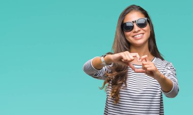 Genç güzel Arap kadın kalp simgesi ve elleriyle şekil gösterilen aşık gülümseyen izole arka plan üzerinde güneş gözlüğü takıyor. Romantik kavramı.