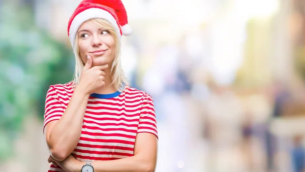 年轻美丽的金发女子戴着圣诞节帽子在孤立的背景与手在下巴思考问题 沉思的表达 微笑着体贴的脸 怀疑概念 — 图库照片