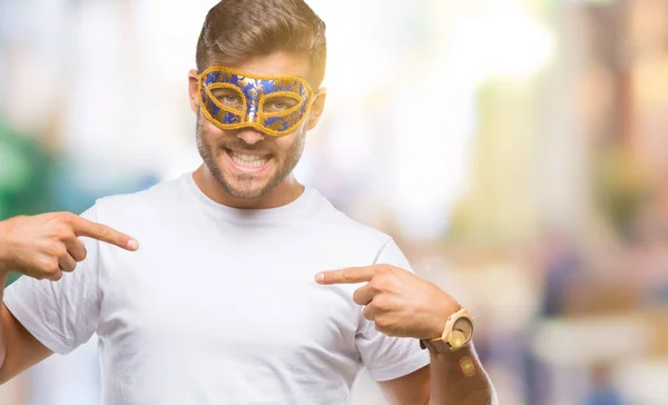 Young handsome man wearing carnival mask over isolated background looking confident with smile on face, pointing oneself with fingers proud and happy.