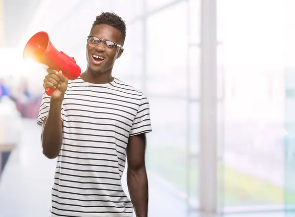 Young african american man holding megaphone with a happy face standing and smiling with a confident smile showing teeth