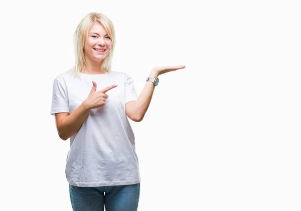 年轻美丽的金发碧眼的女人穿着白色的 T恤在孤立的背景惊讶和微笑的相机 同时提出用手和手指指指点点 — 图库照片