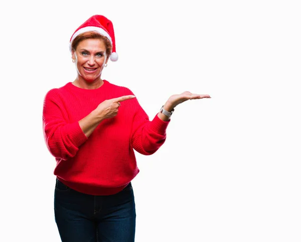 在孤立的背景上戴着圣诞帽的高级高加索红发女郎惊讶地对着镜头微笑 同时用手和手指指指点点 — 图库照片