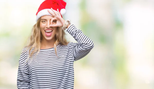 手の笑顔 幸せそうな顔で指を通して見る目で のジェスチャーを行う分離の背景にクリスマス帽子身に着けている美しい若いブロンドの女性 — ストック写真