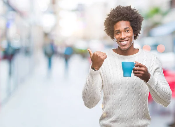 美国黑人男子喝咖啡在孤立的背景指向和显示与幸福的脸微笑的一侧 — 图库照片