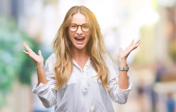 年轻美丽的金发女商人戴着眼镜在孤立的背景庆祝疯狂和惊讶的成功与双臂举起和睁开的眼睛尖叫兴奋 获奖者概念 — 图库照片