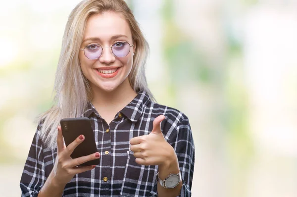 若いブロンドの女性のテキスト メッセージ以上のスマート フォンを使用してメッセージを送信する笑顔の サイン 優秀な兆候を親指をやって幸せなバック グラウンドを分離 — ストック写真