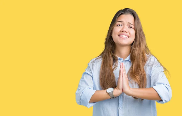 Young beautiful brunette business woman over isolated background begging and praying with hands together with hope expression on face very emotional and worried. Asking for forgiveness. Religion concept.