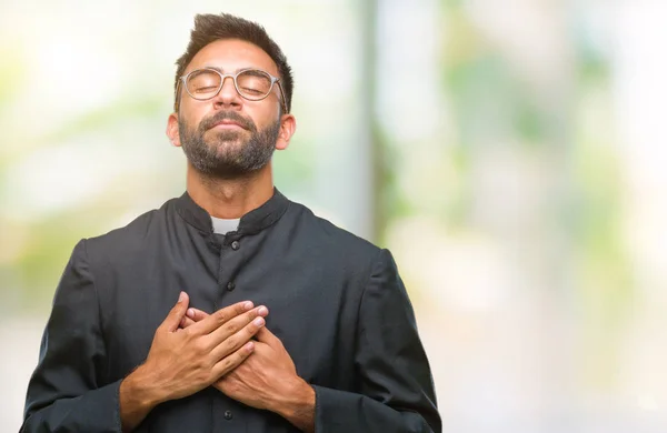 笑みを浮かべて隔離された背景にカトリックの司祭男の手の閉じた目と顔に感謝のジェスチャーの胸に成人ヒスパニック系 健康の概念 — ストック写真