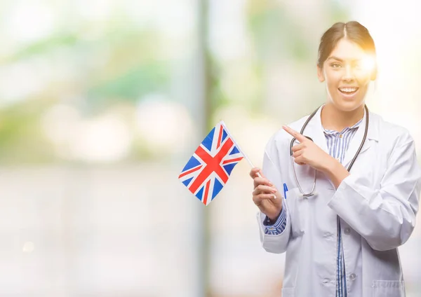 Jovem Médica Hispânica Segurando Bandeira Reino Unido Muito Feliz Apontando — Fotografia de Stock