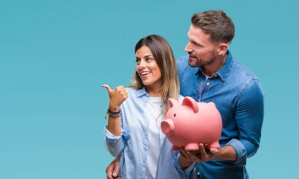 年轻夫妇在爱情持有小猪银行在孤立的背景指向和显示与拇指向上的一面微笑的笑脸 — 图库照片