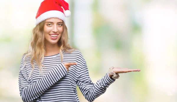 美丽的年轻金发碧眼的女人在孤立的背景上戴着圣诞帽 惊讶地对着镜头微笑 同时用手和手指指指点点 — 图库照片