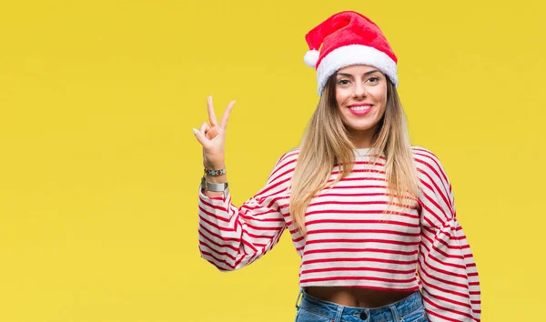 若い美しい女性の勝利のサインを行うカメラでウィンクしている幸せそうな顔を浮かべて隔離された背景にクリスマス帽子をかぶっています — ストック写真