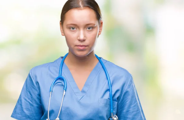 顔に真剣な表情で孤立した背景に医療制服を着て若い白人の医者の女性 シンプルで自然なカメラを見てください — ストック写真