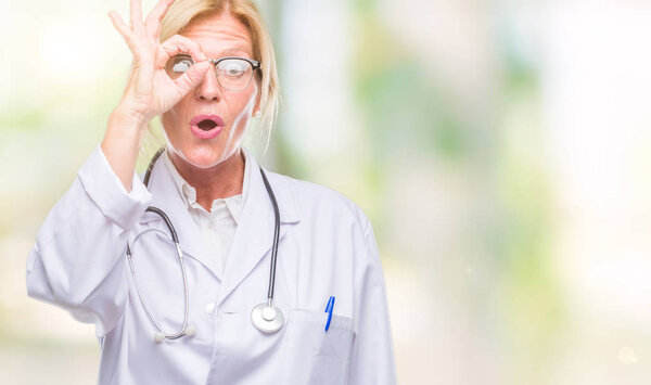 Блондинка средних лет доктор женщина на изолированном фоне делает нормально жест шокирован удивленным лицом, глаза смотрят сквозь пальцы. Неверное выражение
.