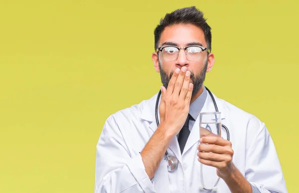 Adult hispanic doctor man drinking glass of water over isolated background cover mouth with hand shocked with shame for mistake, expression of fear, scared in silence, secret concept