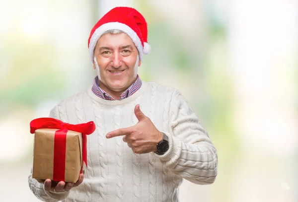 非常に幸せな手と指で指している孤立した背景の上クリスマス帽子 持株ギフトを着てハンサムな年配の男性 — ストック写真
