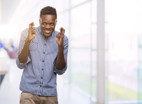 Joven Afroamericano Vestido Con Camisa Azul Sonriendo Cruzando Los Dedos —  Fotos de Stock