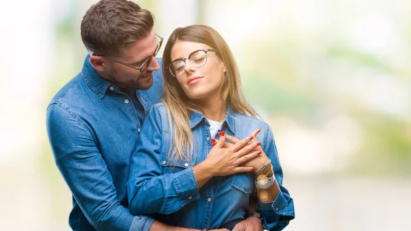 笑みを浮かべて隔離された背景にメガネの愛の若いカップルは 閉じた目と顔に感謝のジェスチャーの胸に手します 健康の概念 — ストック写真