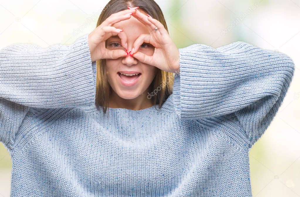 Young beautiful caucasian woman wearing winter sweater over isolated background doing ok gesture like binoculars sticking tongue out, eyes looking through fingers. Crazy expression.