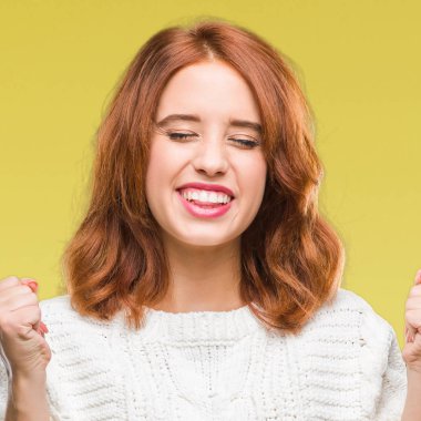 Genç güzel kadın giyiyor kış kazak silah ile başarı için heyecanlı izole arka plan üzerinde zafer kutluyor gülümseyen kaldırdı. Kazanan kavramı.