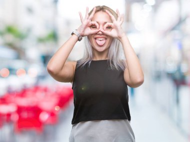 Genç Sarışın kadın dilini, parmaklarının arasından baktığını yapışmasını dürbün gibi ok jest yapıyor izole arka plan yüzünden. Deli ifade.